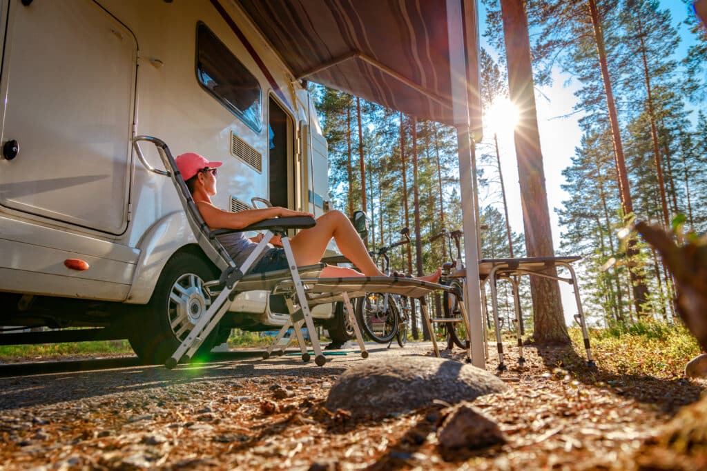 A woman relaxes in a chair in front of an rv.