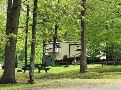 A rv parked in a wooded area with picnic tables.